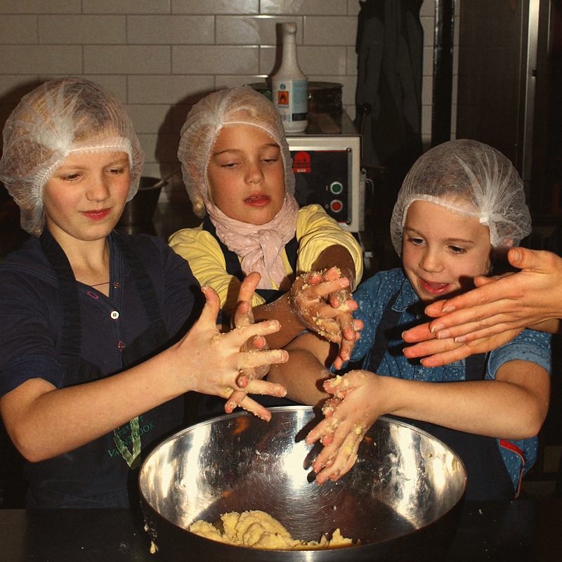 Drei Kinder mit Haarnetz kneten zusammen Teig in einer großen Schüssel