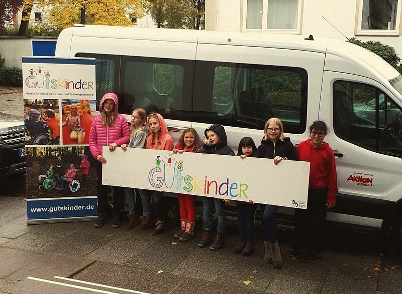 Kinder und Betreuer halten vor dem Vereinsbus ein GutsKinder-Banner hoch