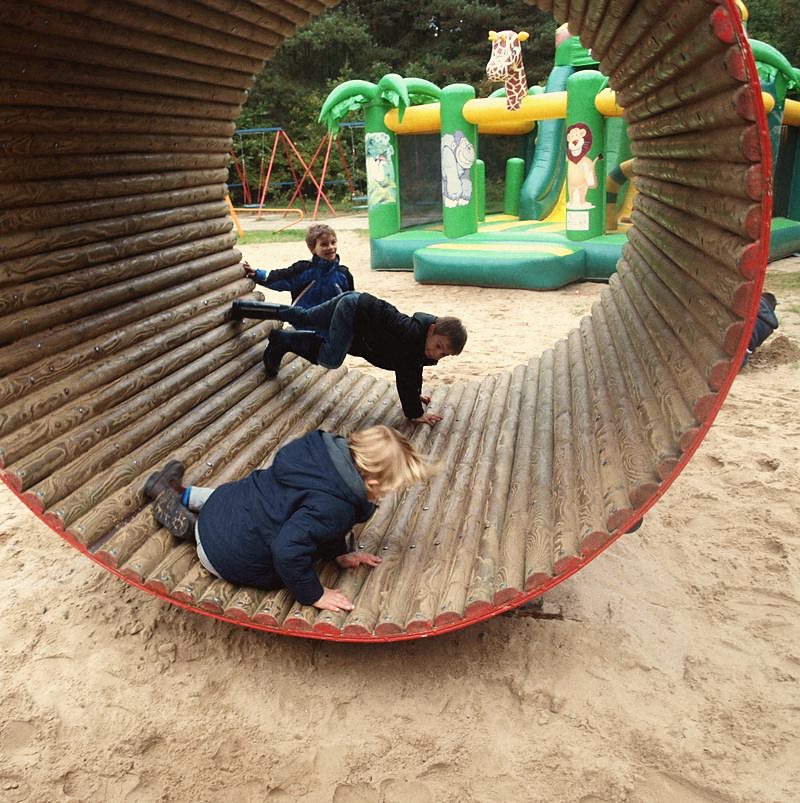 Kinder krabbeln durch eine große hölzerne Kletterröhre auf dem Spielplatz