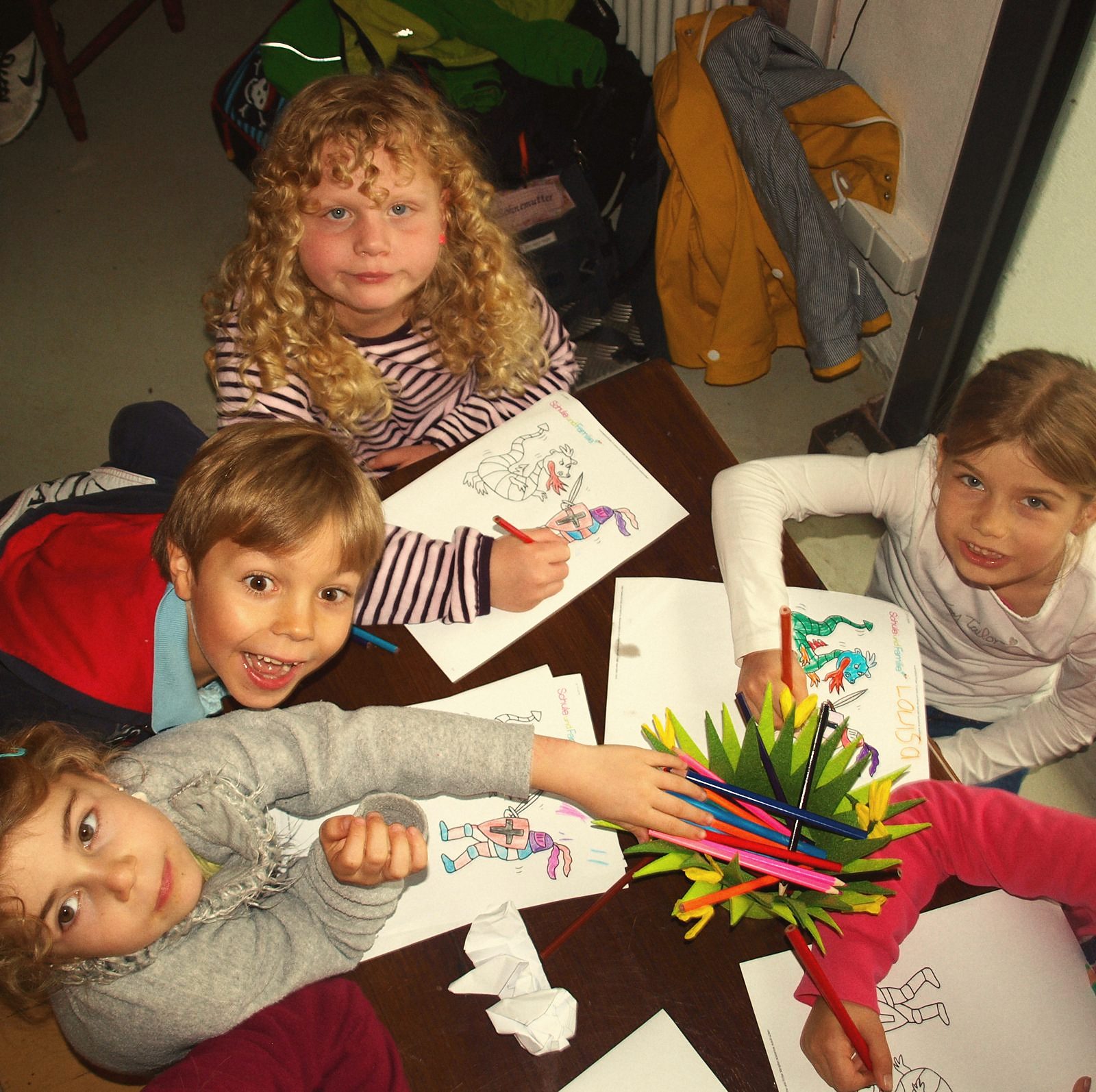 Kinder malen gemeinsam am Tisch und schauen fröhlich in die Kamera