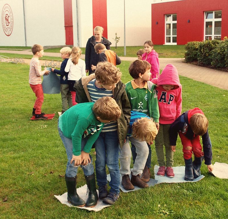 Kinder spielen in Gummistiefeln ein Bewegungsspiel auf der Wiese
