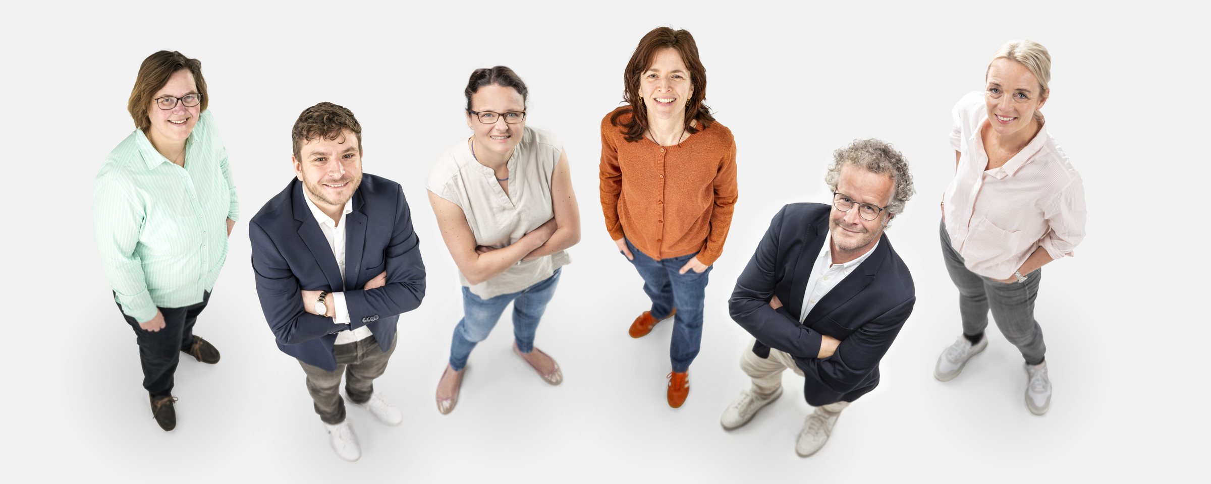 Der Vorstand von GutsKinder e.V. von oben fotografiert: sechs Menschen stehen lächelnd auf hellem Grund und schauen in die Kamera